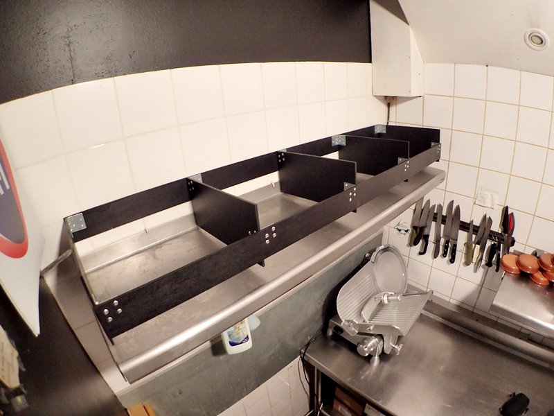 Un rack très léger en contre-plaqué riveté est fixé au mur au-dessus de la planche inox.